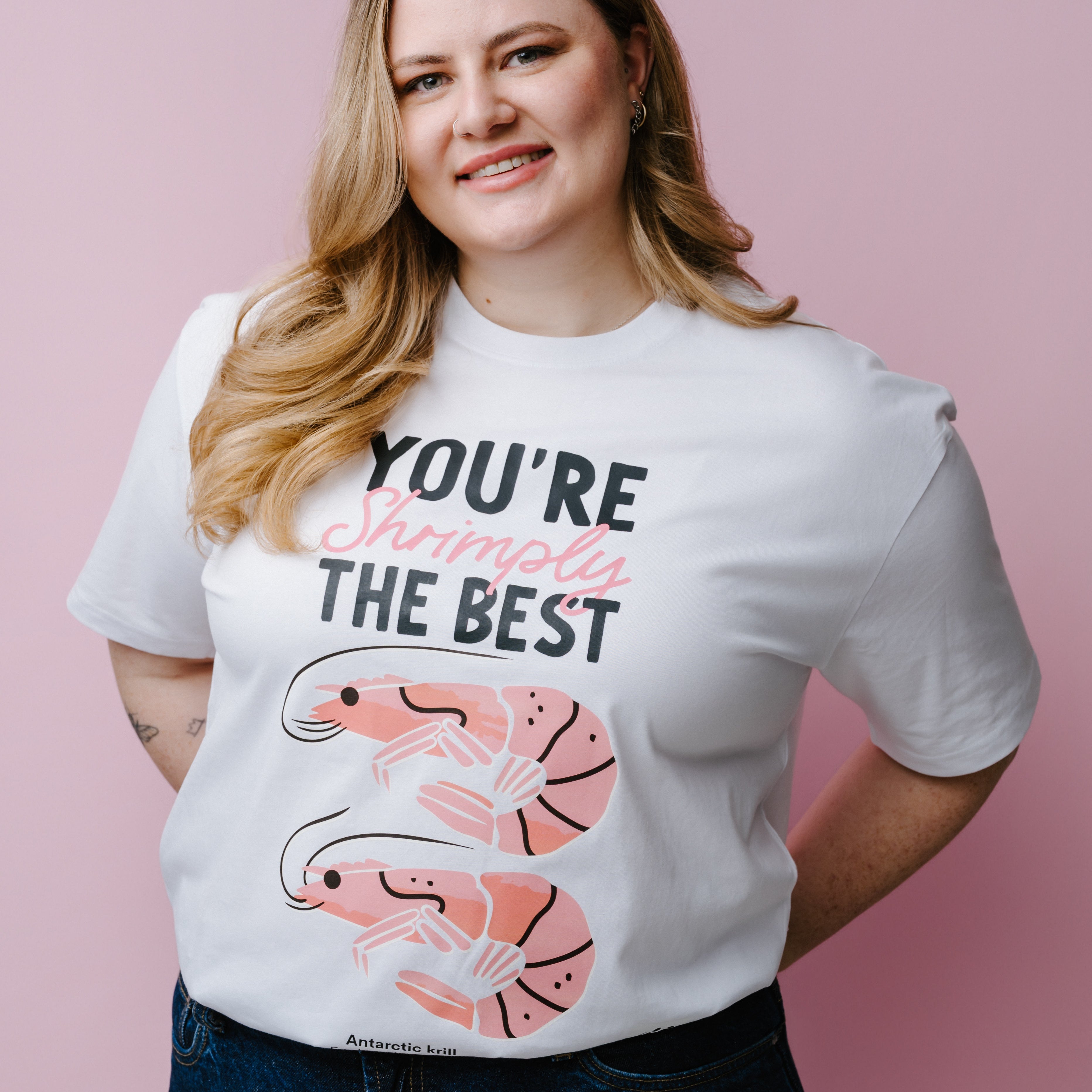 Person wearing a white t-shirt with shrimp graphics and text, "You're Shrimply The Best" against a pink background. Product is a WWF-Australia T-Shirt.
