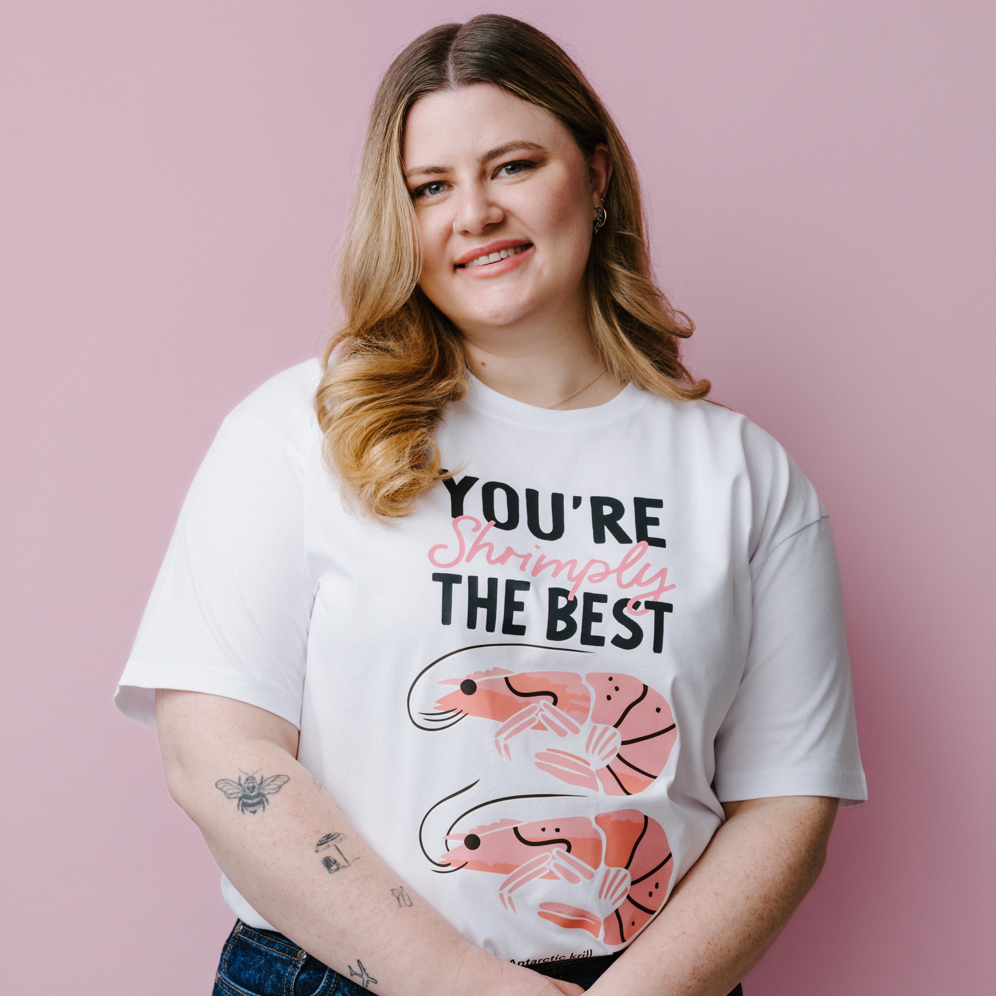 Person wearing a white t-shirt with shrimp graphics and text, "You're Shrimply The Best" against a pink background. Product is a WWF-Australia T-Shirt.