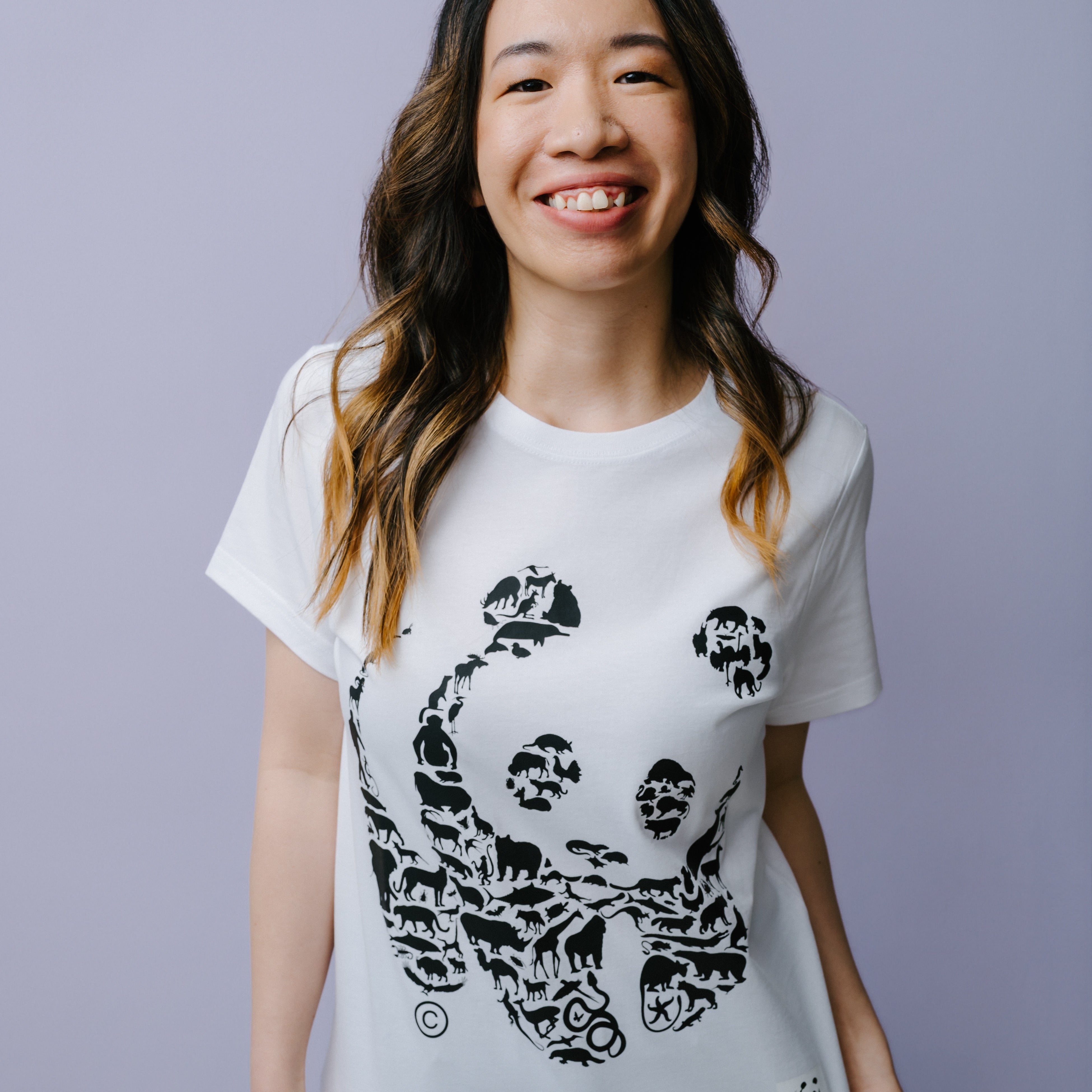 Woman wearing a white t-shirt with a black WWF panda design on a light purple background.