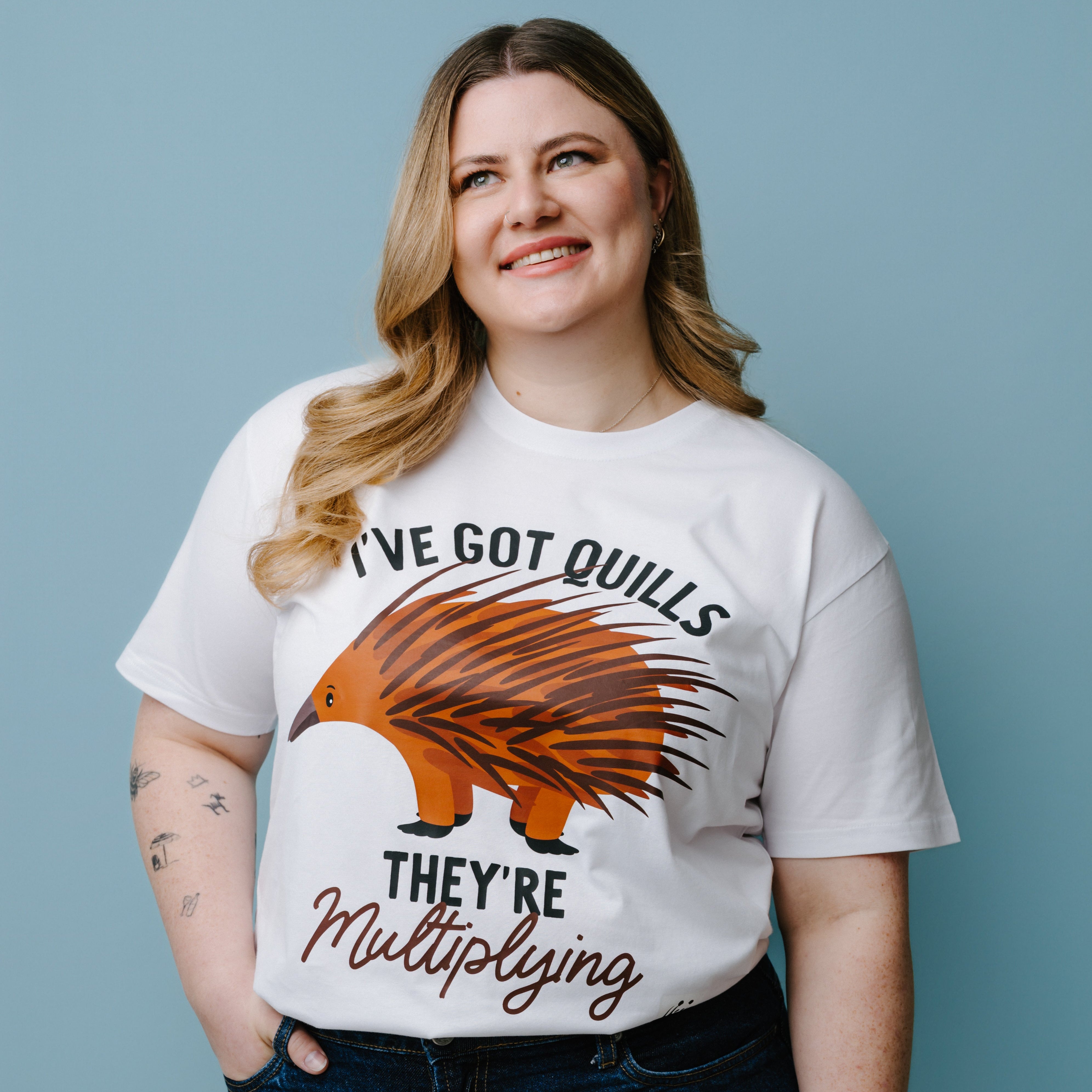 Person wearing a white t-shirt with a graphic of an echidna and text, "I've Got Quills They're Multiplying" against a blue background. The product is a WWF-Australia T-Shirt.