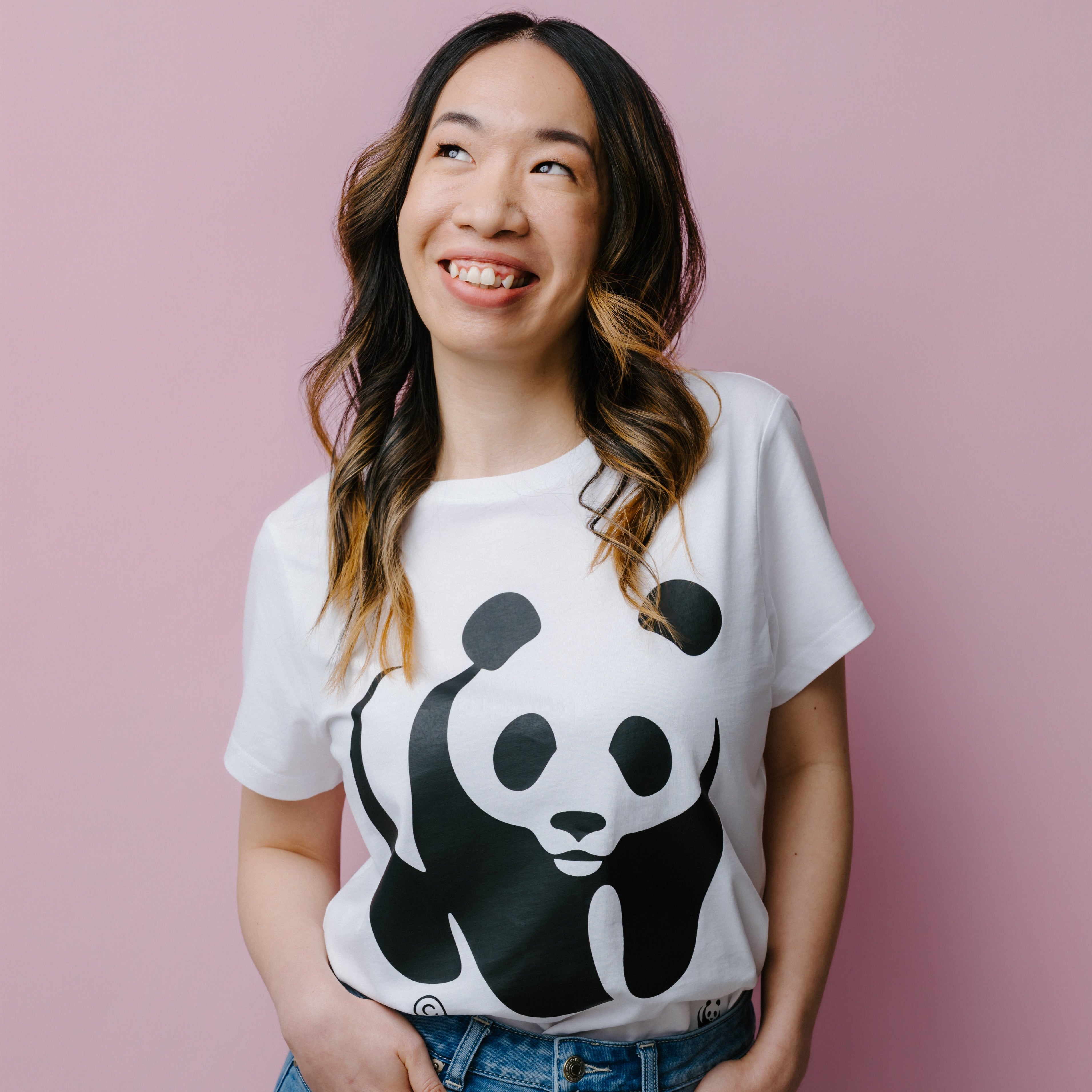 A person wearing a white WWF Panda logo t-shirt against a pink background.