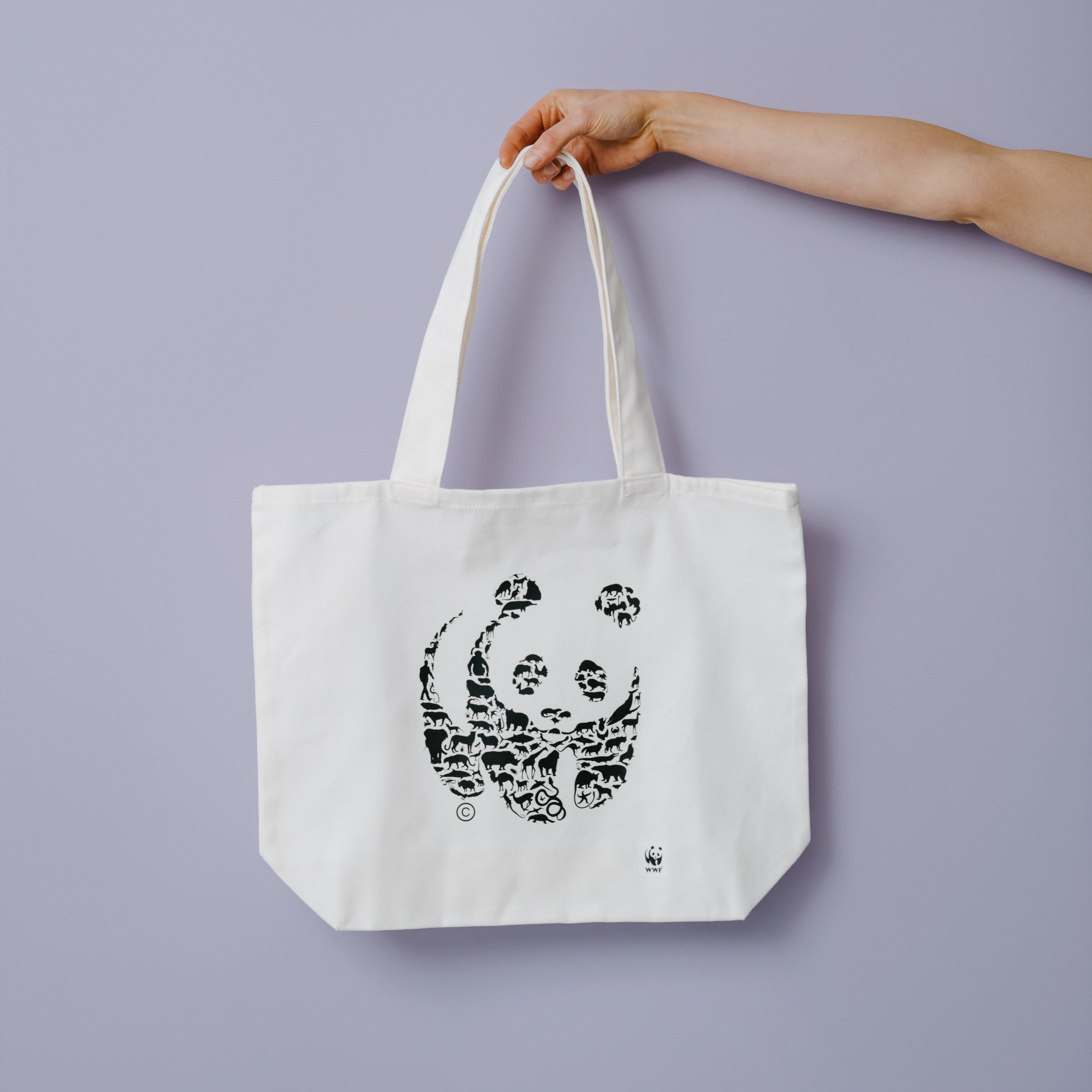 Tote bag with a WWF panda lgoo design held by a hand against a purple background
