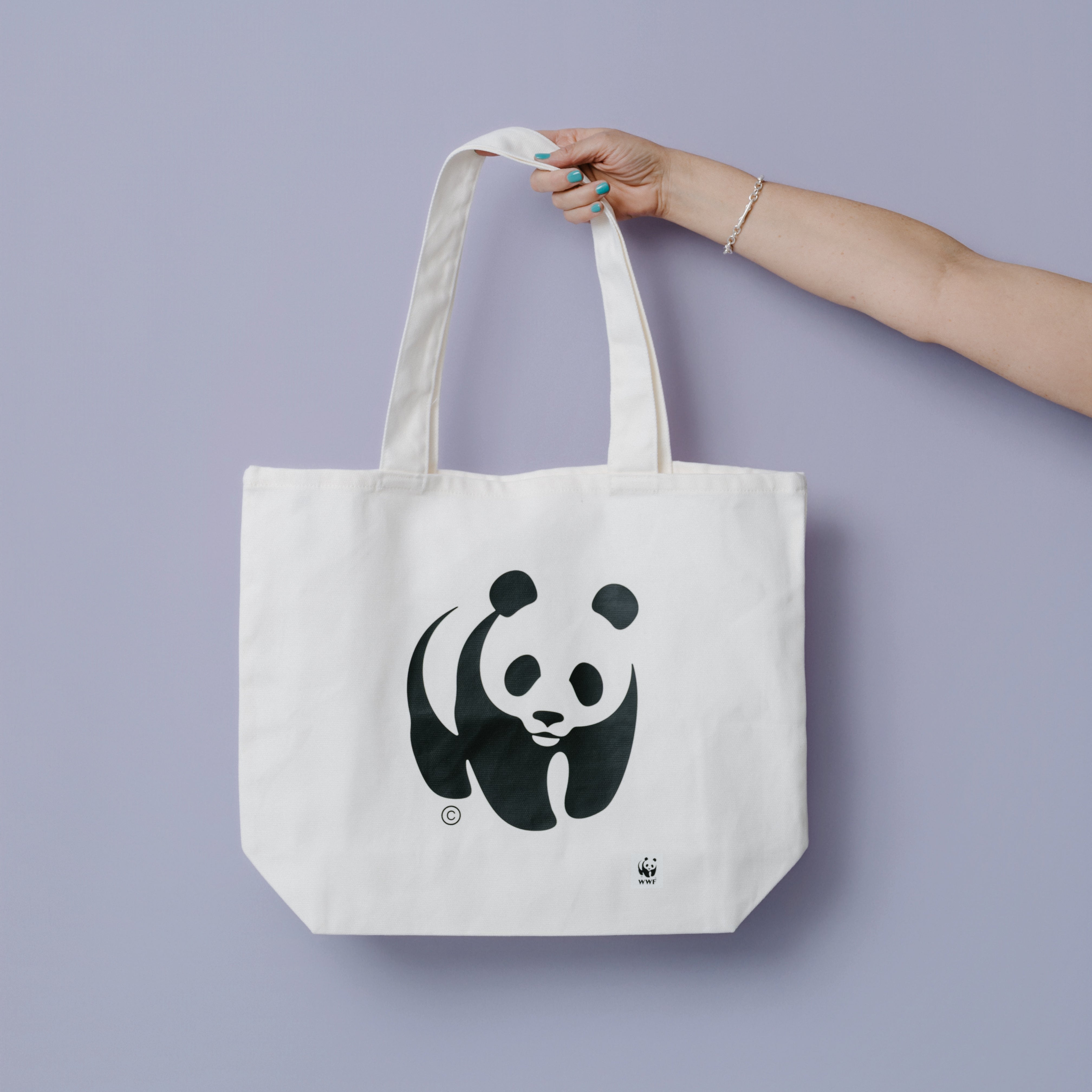Tote bag with WWF-Australia panda logo design held by a hand against a light purple background