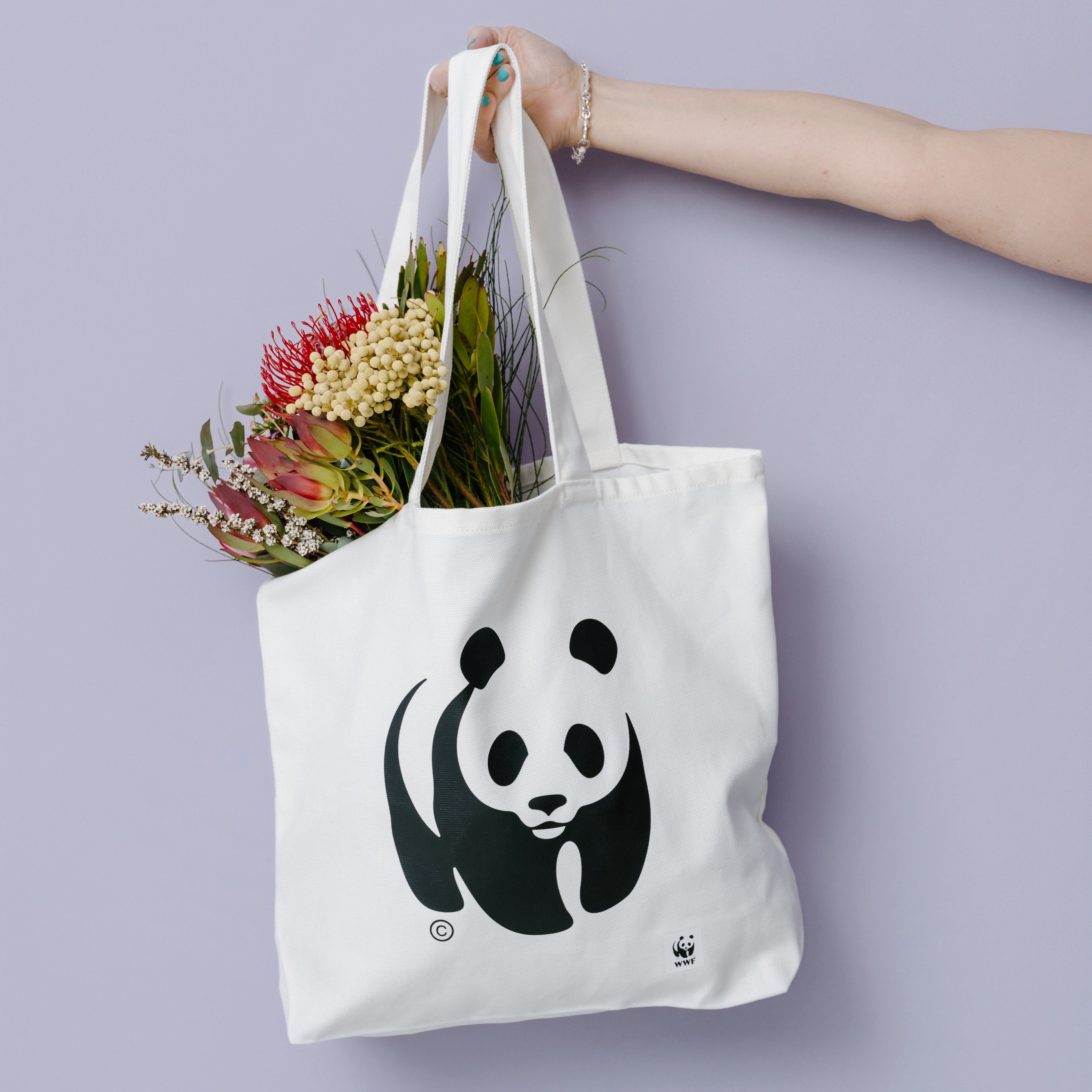 White tote bag with panda design held by a hand against a light purple background