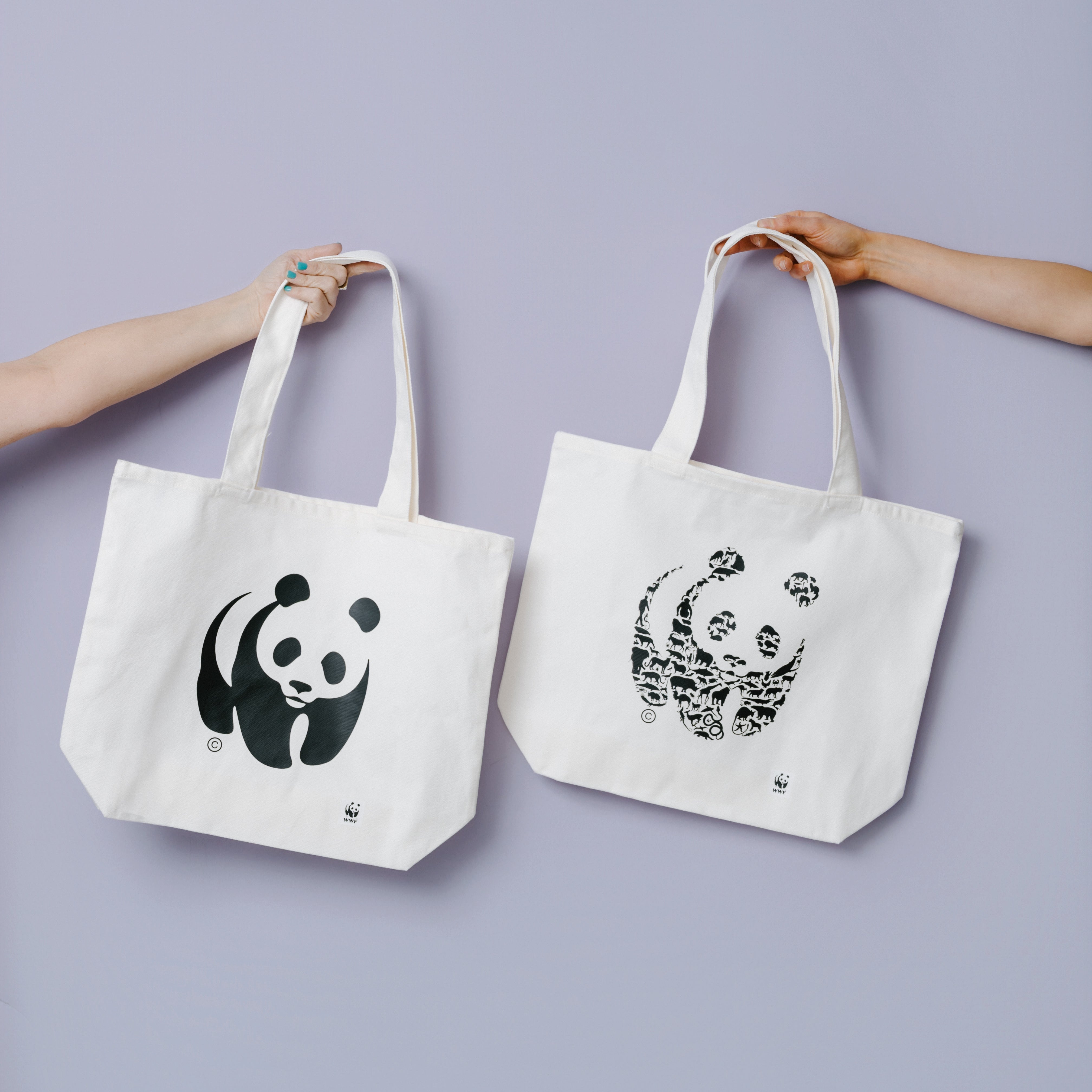 photo of two hands holding out cream WWF-AUstralia panda logo tote bags against a lilac background. Credit: BREEANA DUNBAR